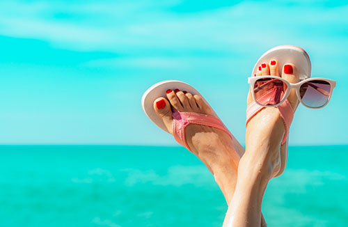Upside woman feet and red pedicure wearing pink sandals, sunglasses at seaside. Funny and happy fashion young woman relax on vacation. Chill out girl at beach. Creative for tour agent. Weekend travel.
